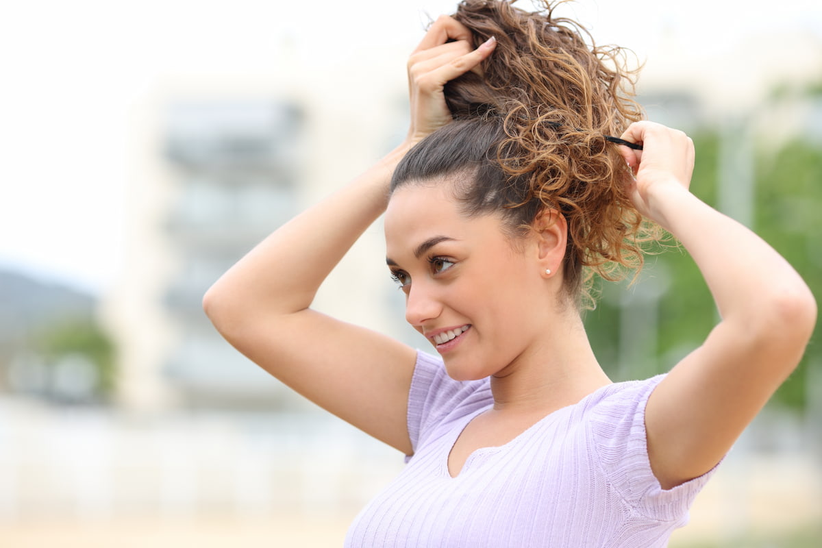 Woman standing outside and putting her curly hair in ponytail